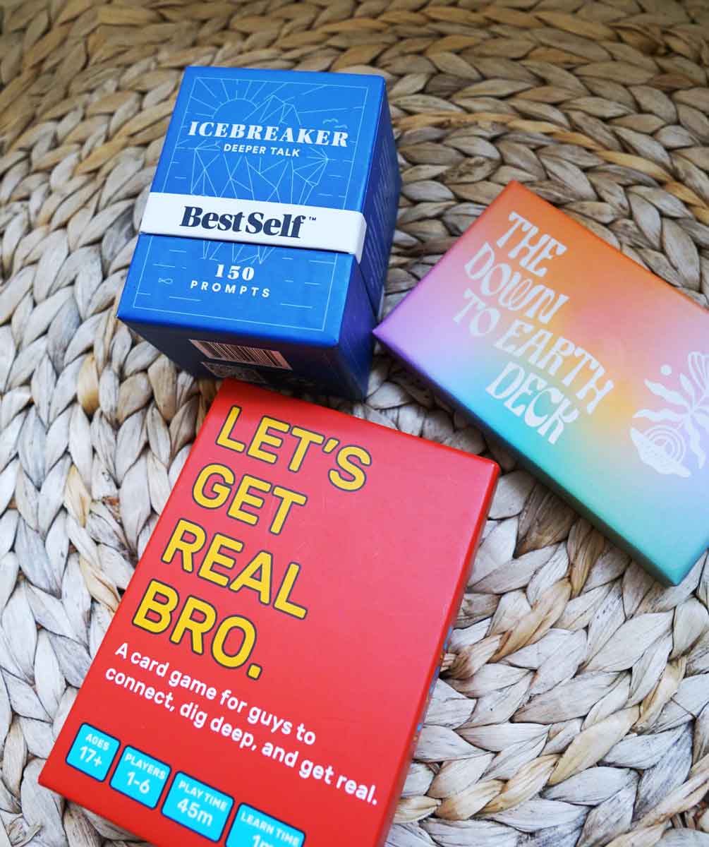 Drie decks gesprekskaarten die naast elkaar zitten: BestSelf's Icebreaker Deeper Talk Deck, LOAM's The Down To Earth Deck en Let's Get Real Bro