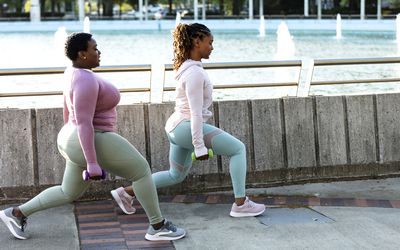 Twee Afro-Amerikaanse vrouwen die samen sporten in een stadspark, bij een grote fontein aan de waterkant van de stad.