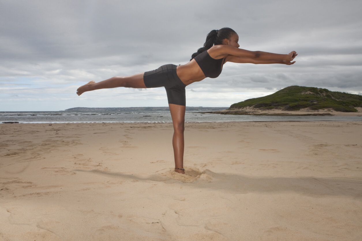 Foto van een vrouw die yoga beoefent op het strand.