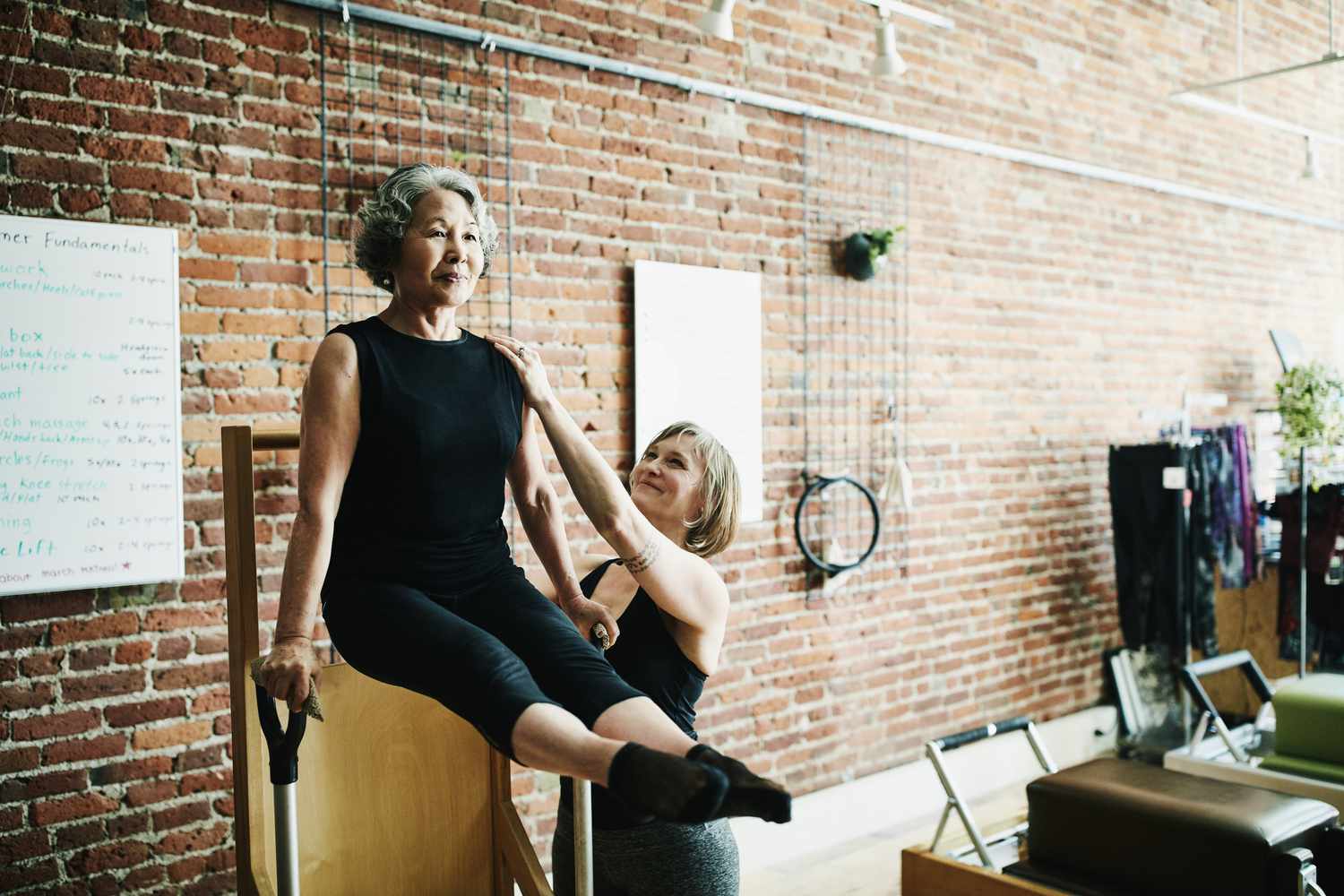Vrouwelijke pilates-instructeur die volwassen student op hoog-laag stoel assisteert tijdens de les in de oefenstudio