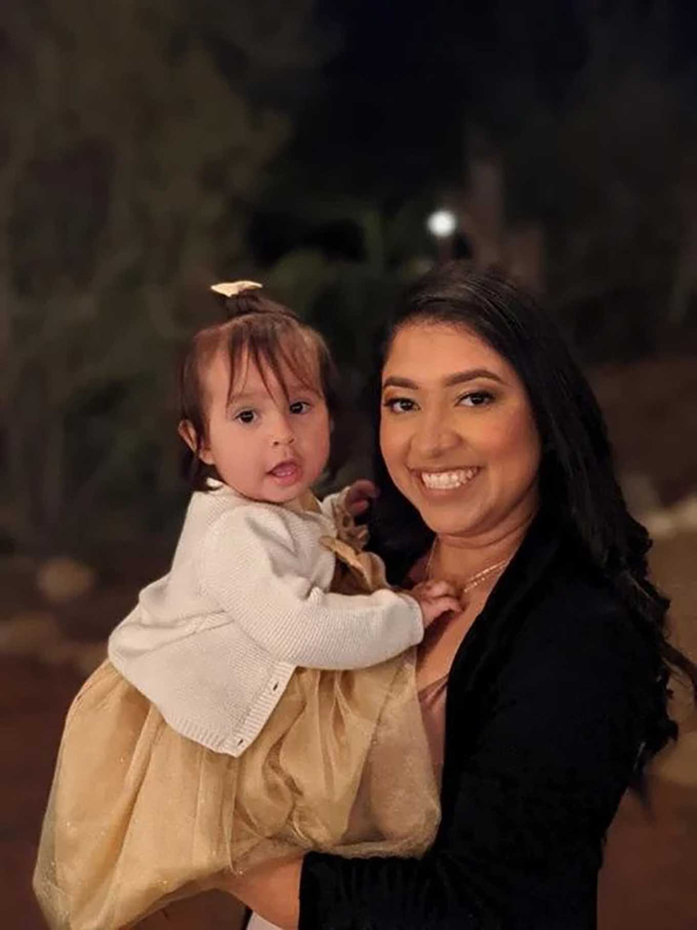 Een moeder glimlacht naar de camera terwijl ze haar baby in haar armen houdt.