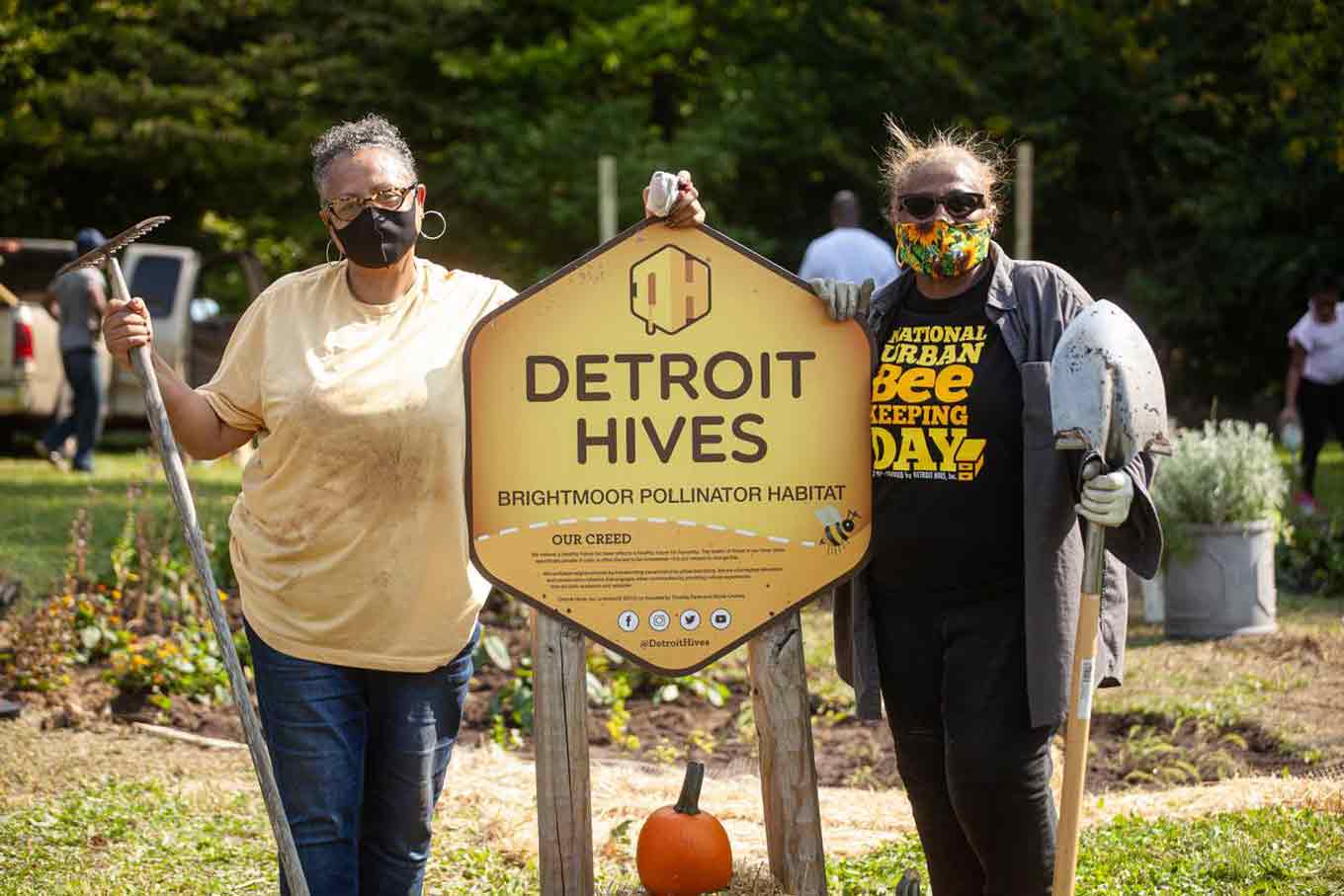 Twee vrouwen poseren met landbouwmachines met een "Detroit Bijenkorven" teken tussen hen in