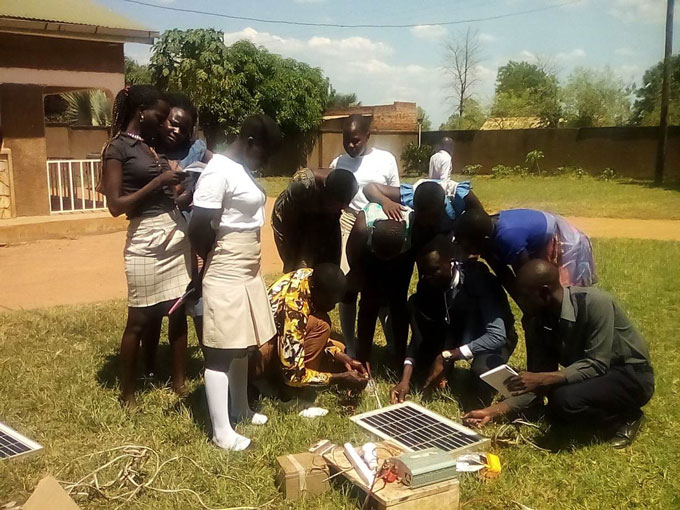Mensen verzamelen zich rond een zonnepaneel tijdens een trainingssessie van BOSCO in Kitgum in Oeganda.