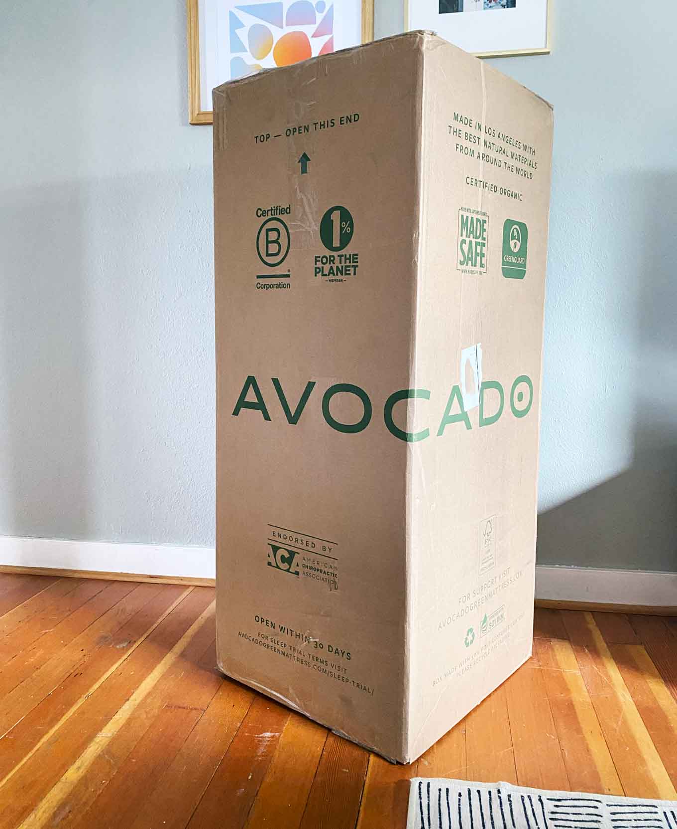 Doos voor Avocado eco biologische matras, voor het uitpakken. De doos heeft logo's voor Certified B Corporation, 1% voor the Planet, Made Safe, Certified Organic en meer...