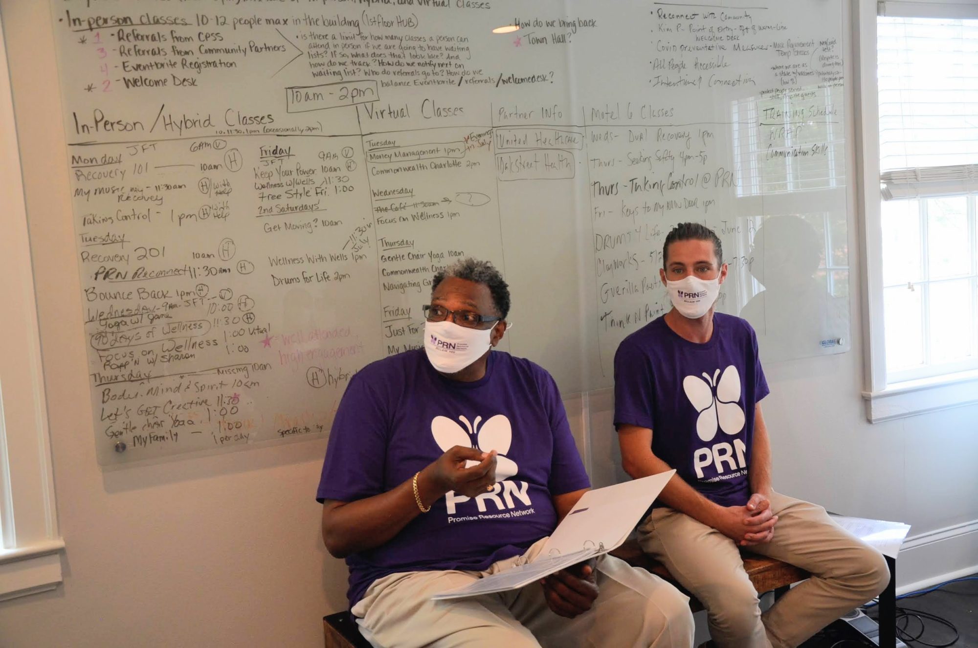 Twee peer support specialisten zitten voor een white board, met papieren in de hand