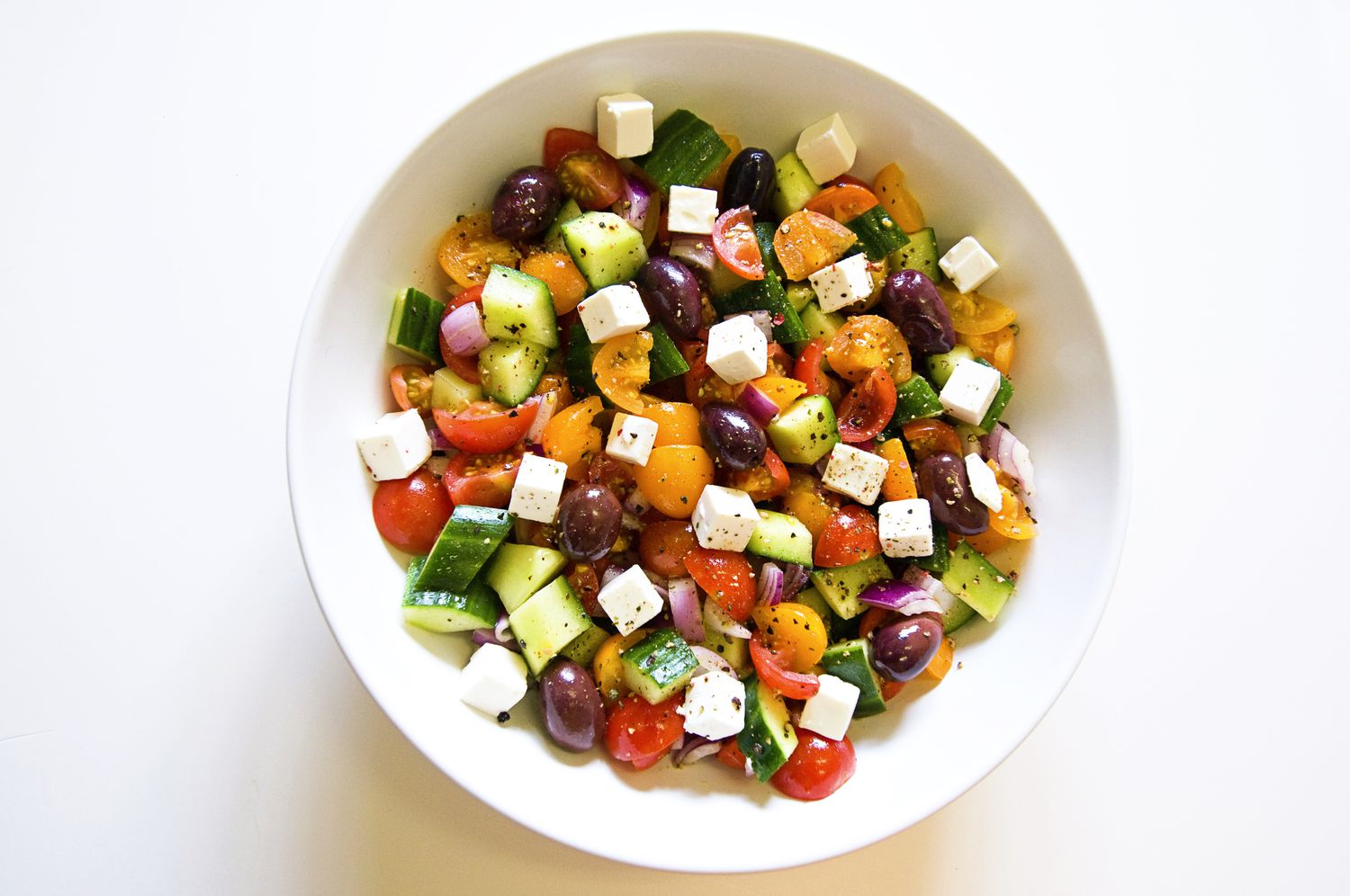 Close-up, high-key afbeelding van een witte kom gevuld met een Griekse salade, inclusief tomaten, komkommer, olijven, uien en fetabonen - stockfoto