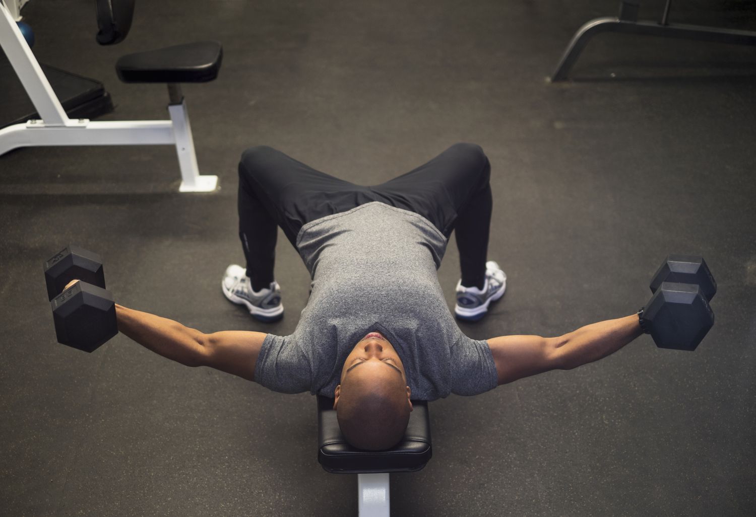 Man die op een gewicht ligt en dumbbell-vliegen doet