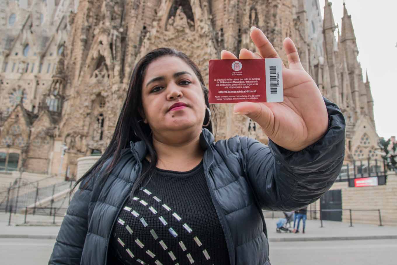 Teresa houdt haar bibliotheekkaart vast terwijl ze naar de camera kijkt met de kathedraal La Sagrada Familia achter haar