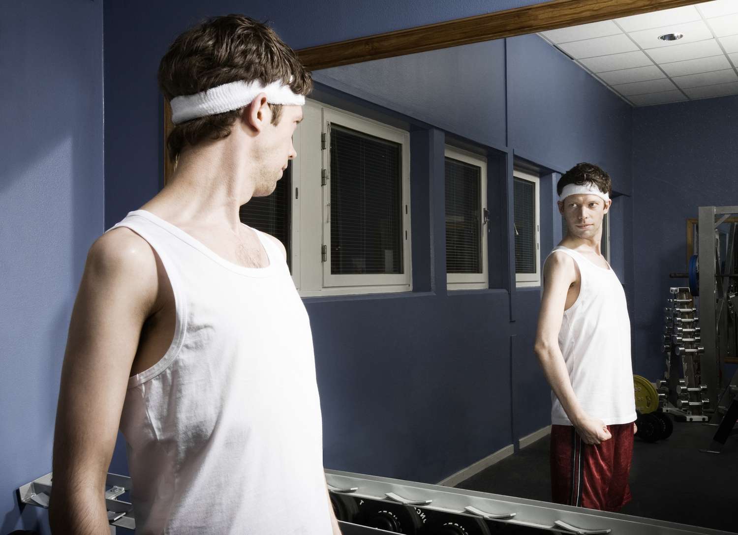 Man met zweetband die naar reflectie in de spiegel van de sportschool kijkt, buigarm