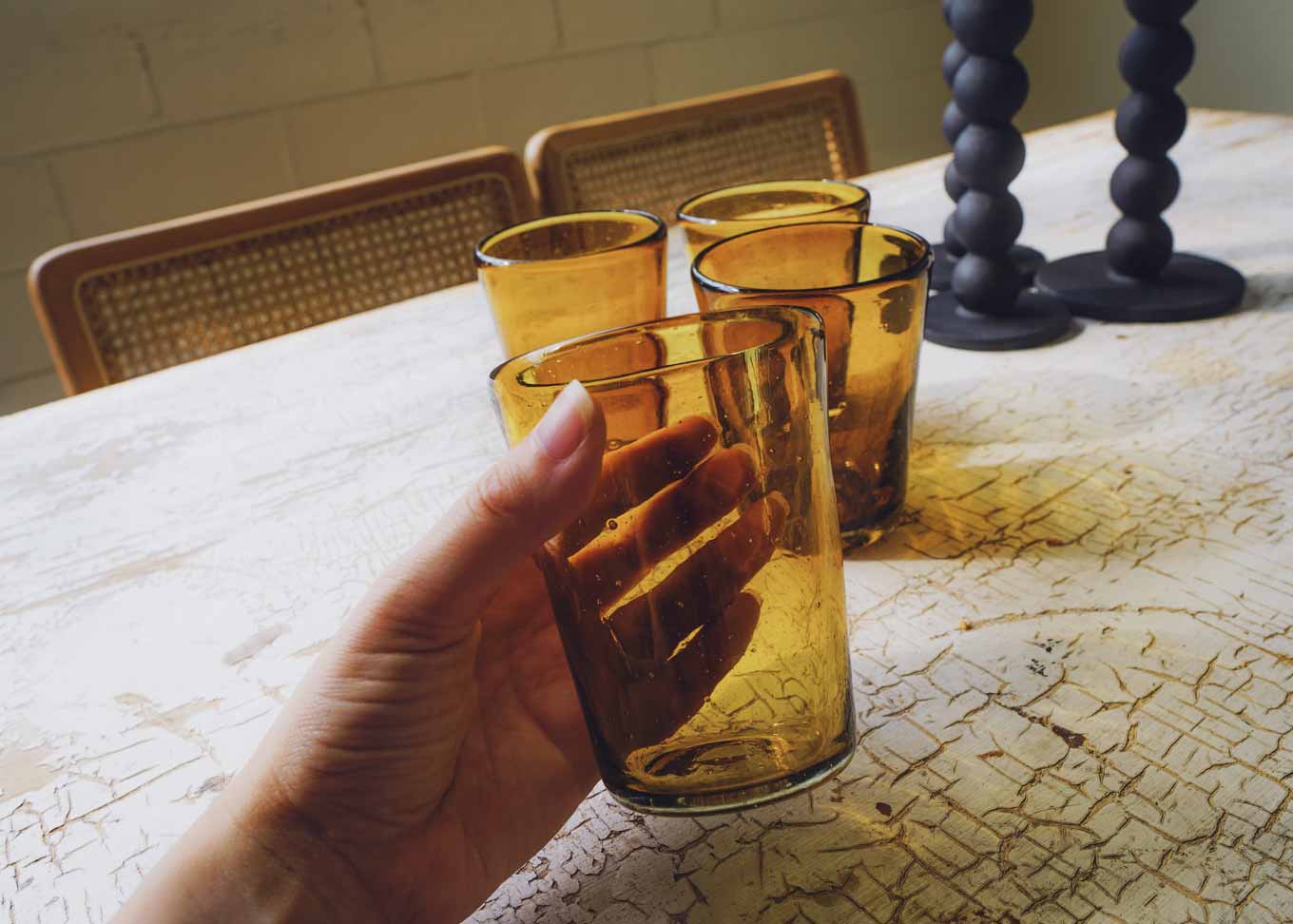 Een amberkleurig handgeblazen gerecycled drinkglas vasthouden aan een tafel