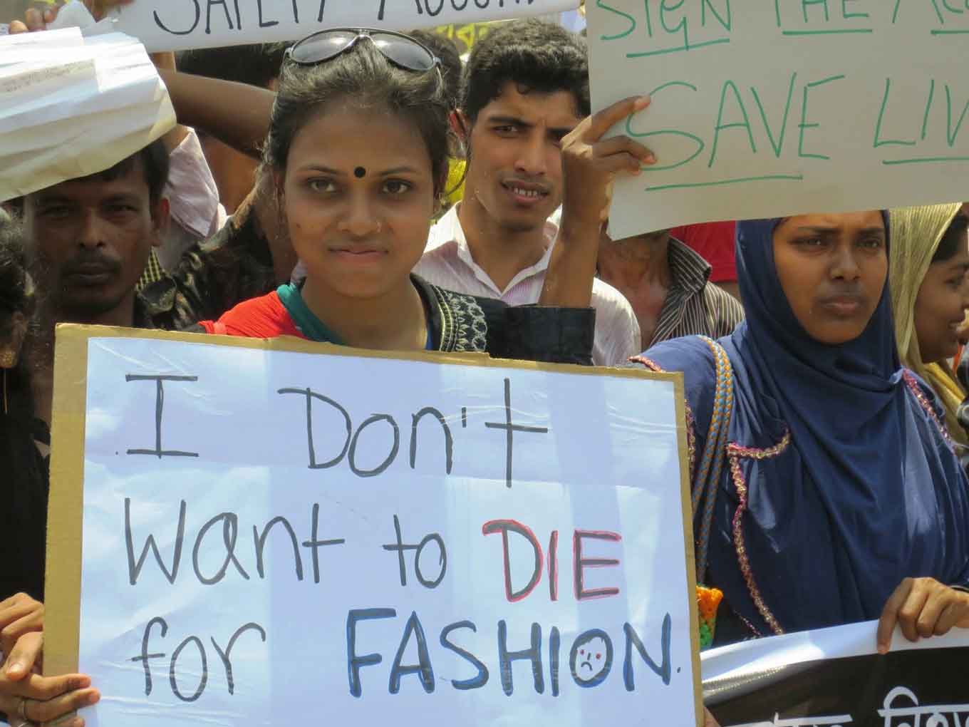 Een vrouw in Bangladesh staat in een menigte met een bord dat zegt: "Ik wil niet STERVEN voor MODE"