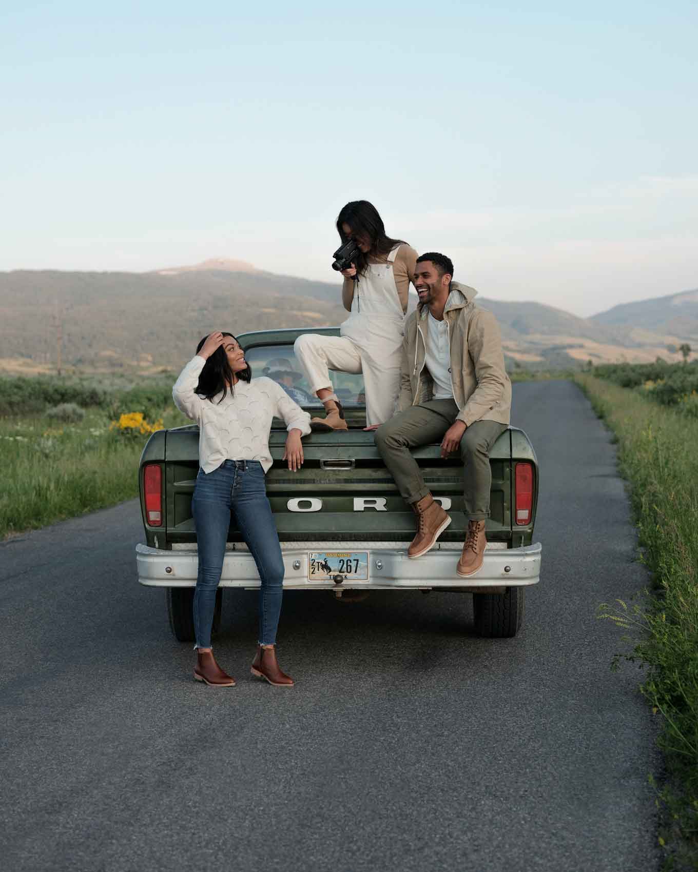 Twee vrouwen en een man poseren en maken foto's van elkaar op een achterkant van een vintage vrachtwagen op een landweggetje, met ethisch gemaakte kleding en schoenen uit Nisoloo