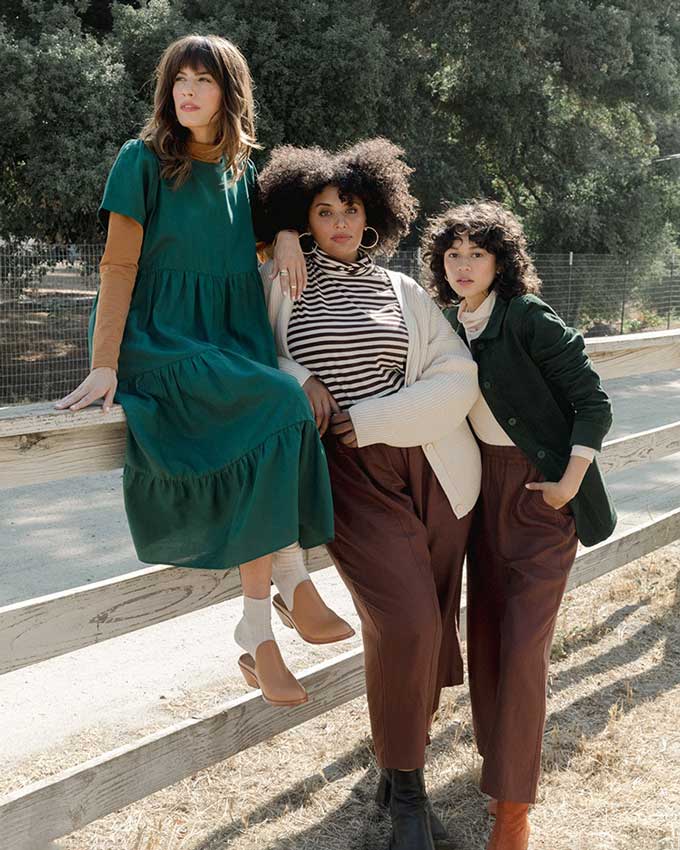 Drie vrouwen die op/bij een hek zitten, dragen stijlvolle, ethisch gemaakte kleding uit Tradlands