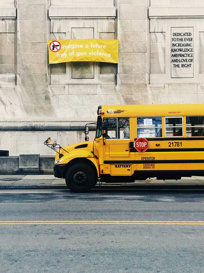 Een spandoek luidt: "Stel je een toekomst voor zonder wapengeweld" — vlak naast een gele schoolbus