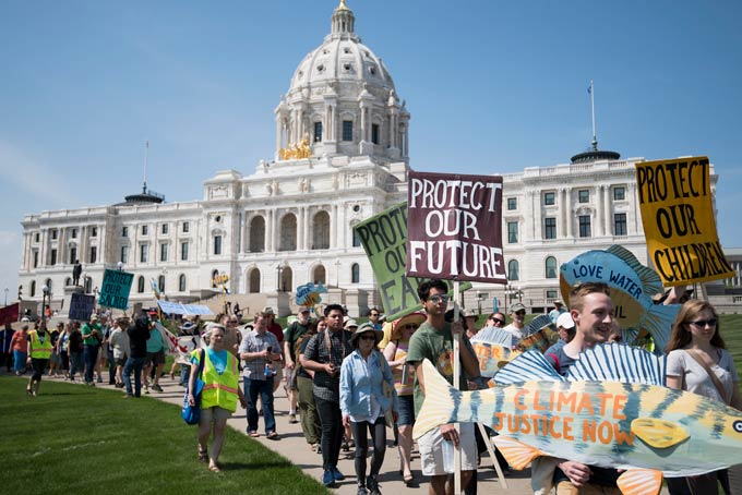 Een menigte mensen marcheert naar het capitool van Minnesota, met borden als "Bescherm onze toekomst", "Bescherm onze kinderen", "Klimaatrechtvaardigheid nu"en "Bescherm onze aarde"