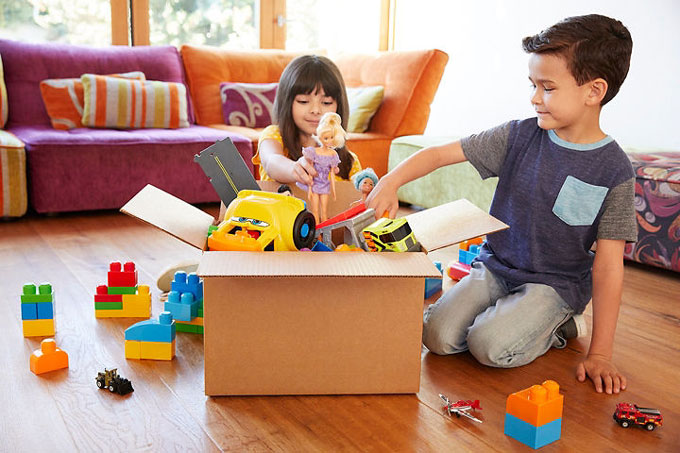 Twee kinderen stoppen hun oude speelgoed in een kartonnen doos