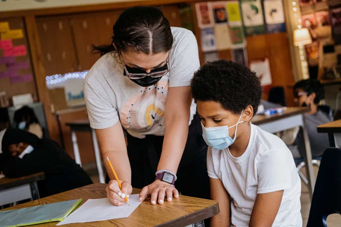 Een leraar helpt een leerling terwijl beiden mondkapjes dragen