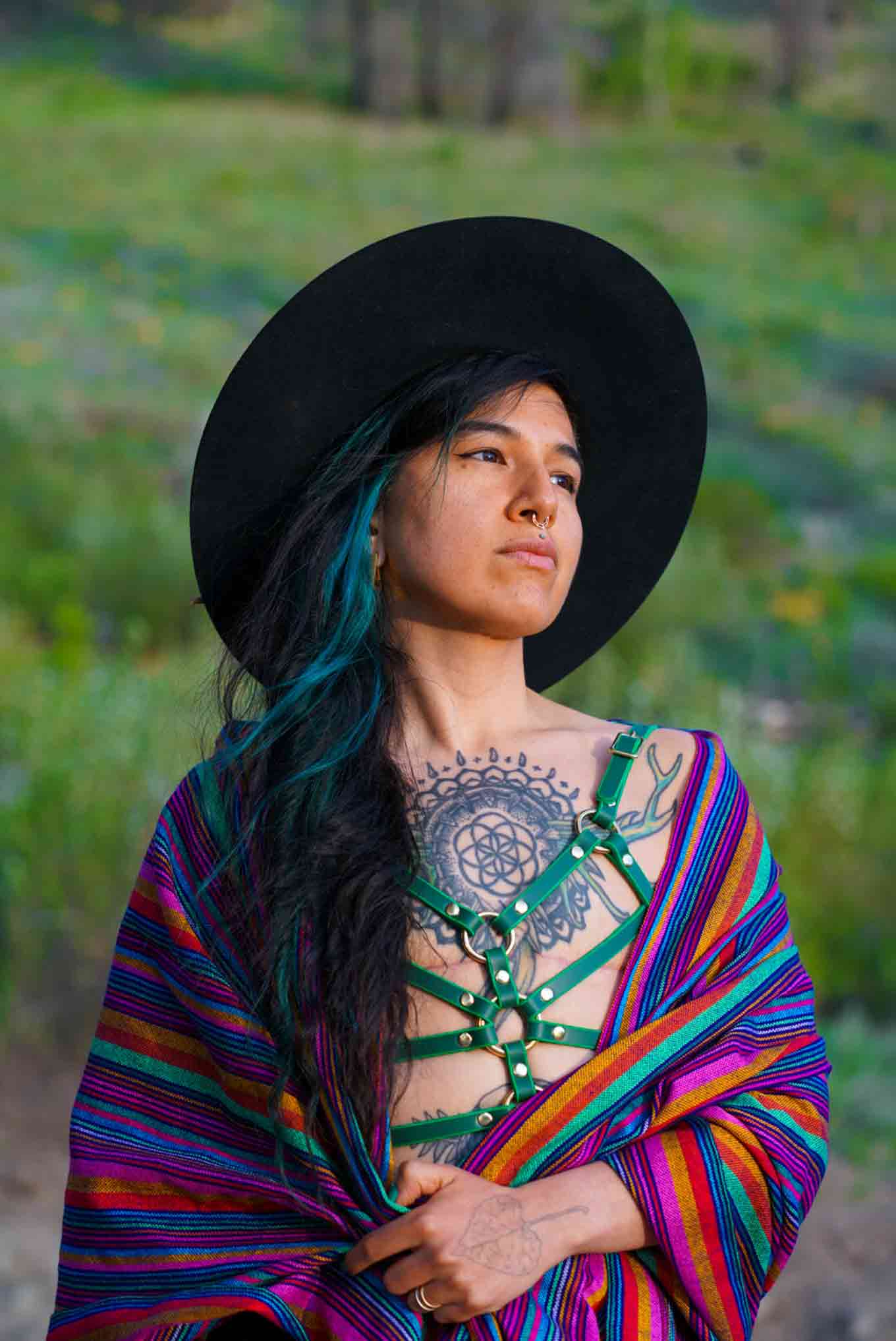 Portret van Pınar Sinopoulos-Lloyd, mede-oprichter van Queer Nature. Ze dragen een zwarte hoed, kleurrijke sjaal met een peinzende uitdrukking.
