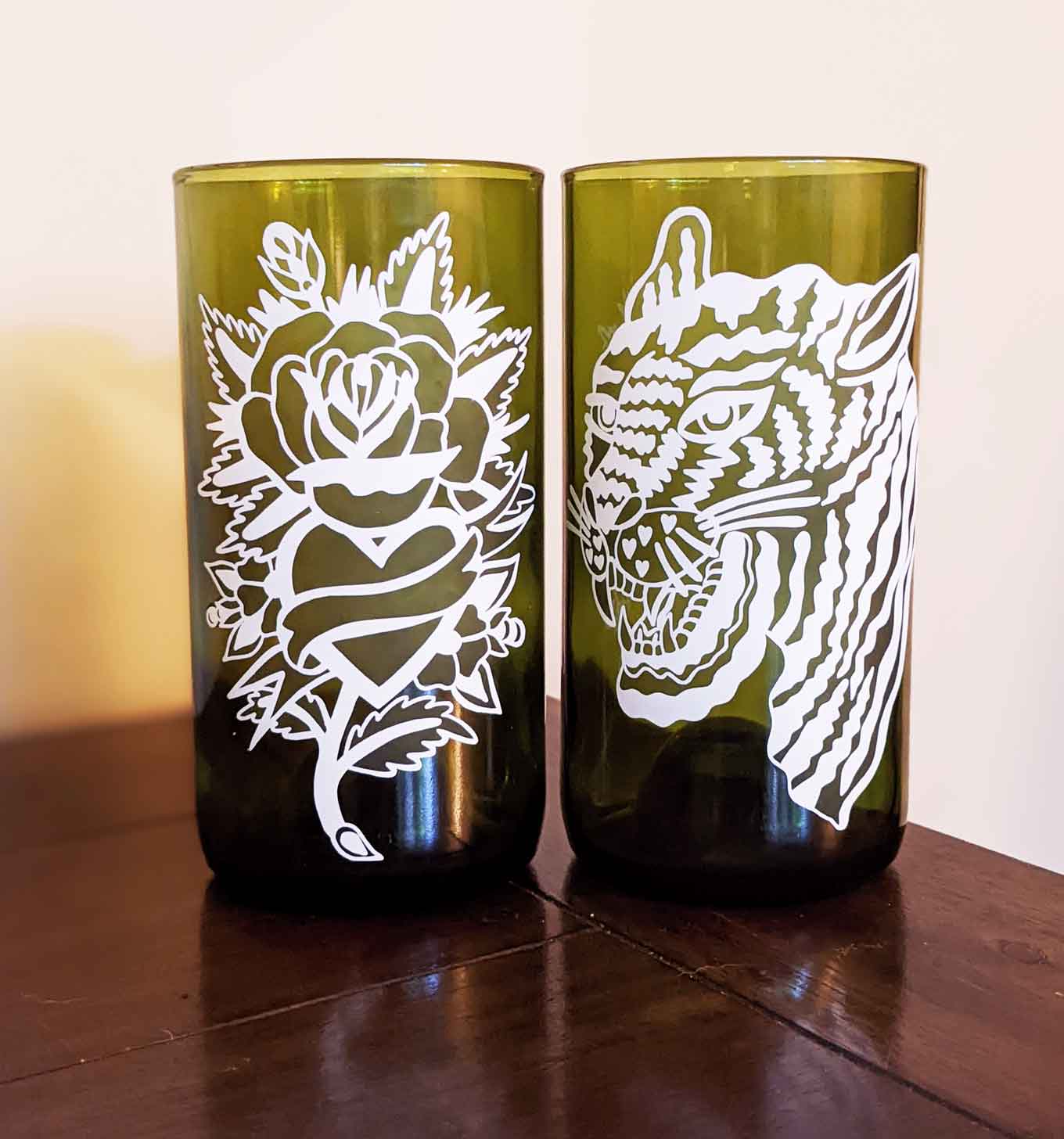 Twee groene gerecyclede glazen, een met een bloemmotief erop gedrukt en een andere met een tijgerontwerp
