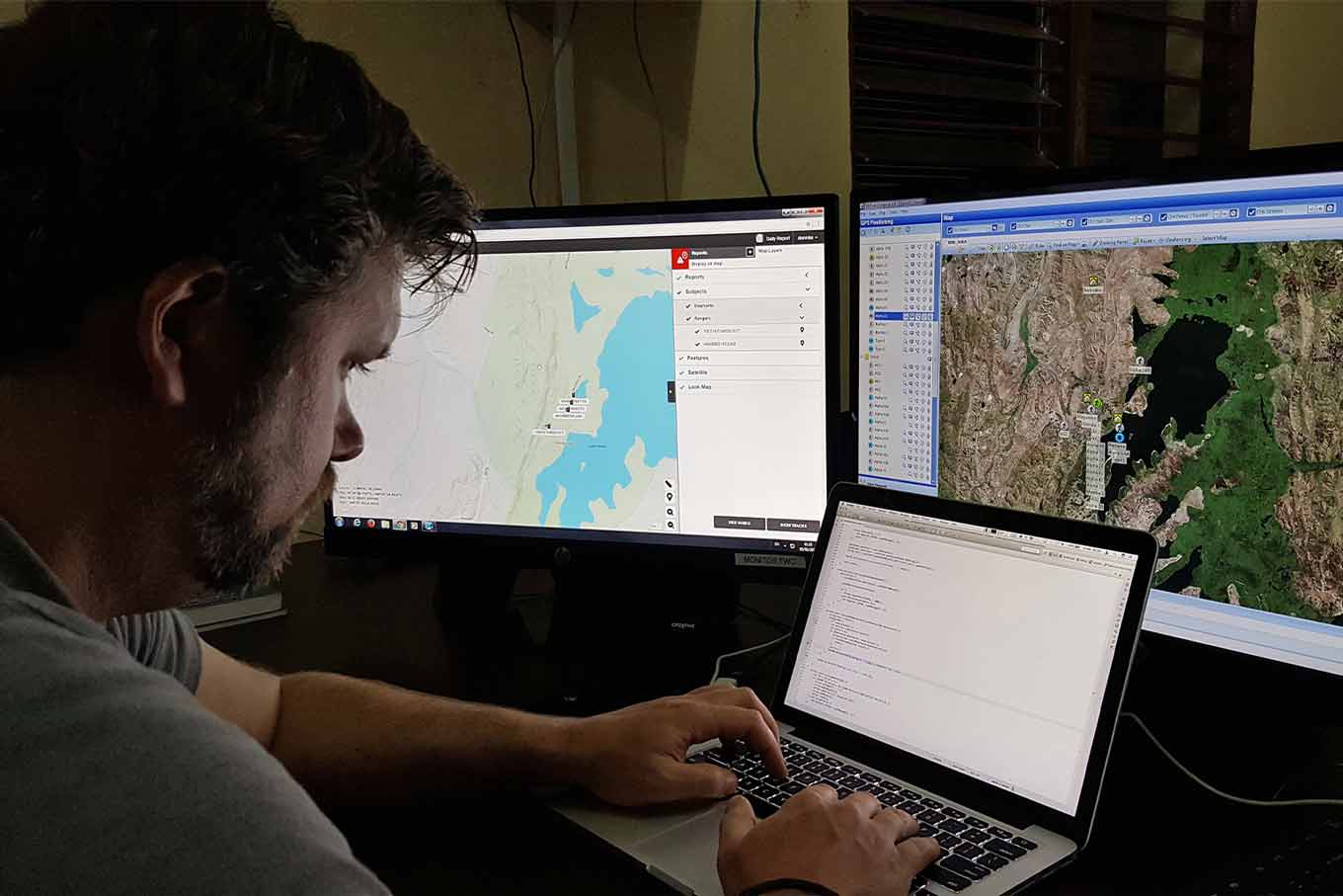 Een man werkt op een laptop met daarachter twee monitoren. 