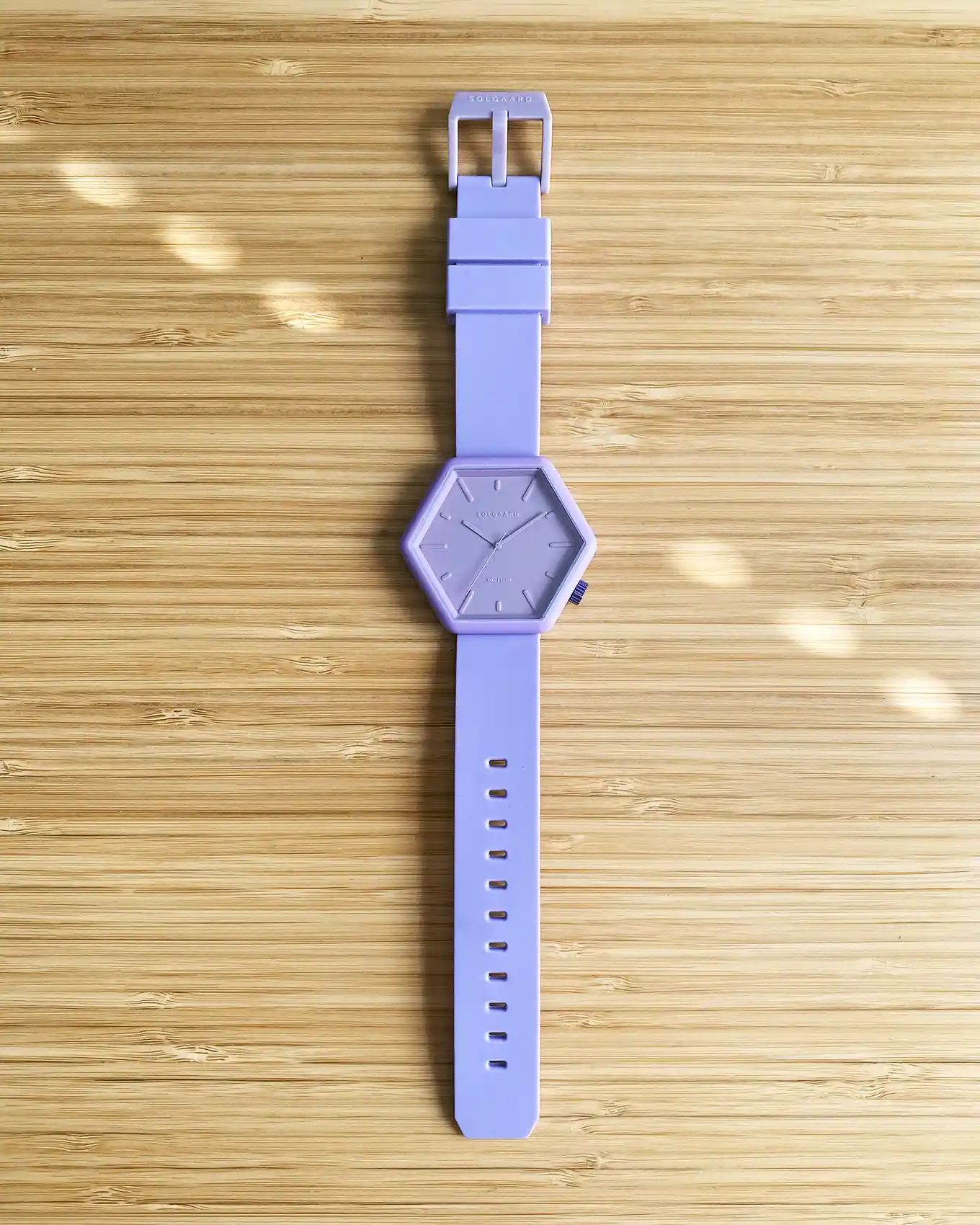 Minimalistisch zeshoekig horloge in een lila kleur, plat op een tafel