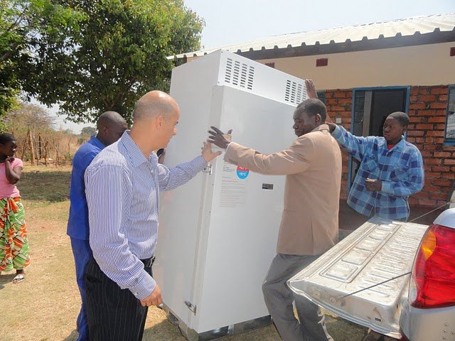 Een groep mensen laadt een witte Surechill-koelkast (gebruikt om vaccins veilig en koud te houden) van een vrachtwagen en in een Afrikaanse medische kliniek