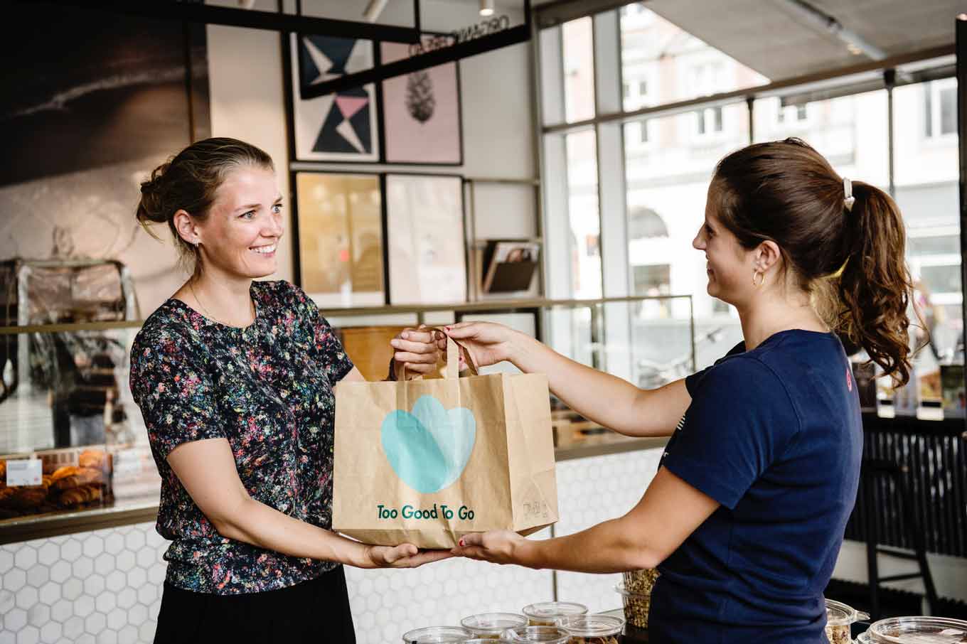 Een winkelmedewerker overhandigt een Too Good To Go 'Surprise Bag' aan een klant