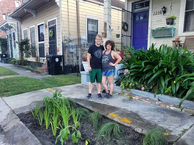 Twee mensen staan vrolijk voor een regentuin bij een huis in New Orleans.