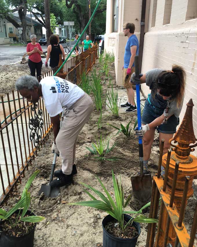Water Wise-vrijwilligers planten inheemse Louisiana-planten in een regentuin tussen een gebouw en een trottoir