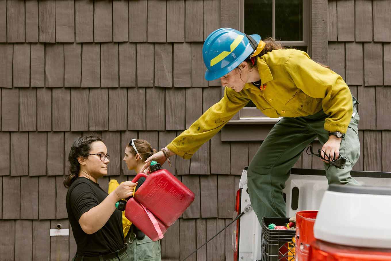 Een vrouwelijke brandweerman bovenop een pick-uptruck geeft twee containers door aan een andere brandweerman in haar buurt