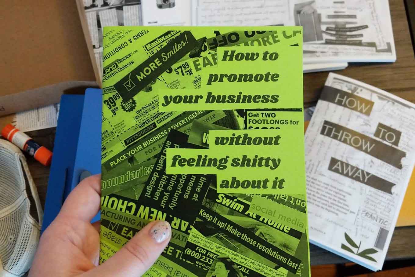 Een hand houdt een kopie van de zine omhoog: "Hoe u uw bedrijf kunt promoten zonder u er schijt aan te voelen."