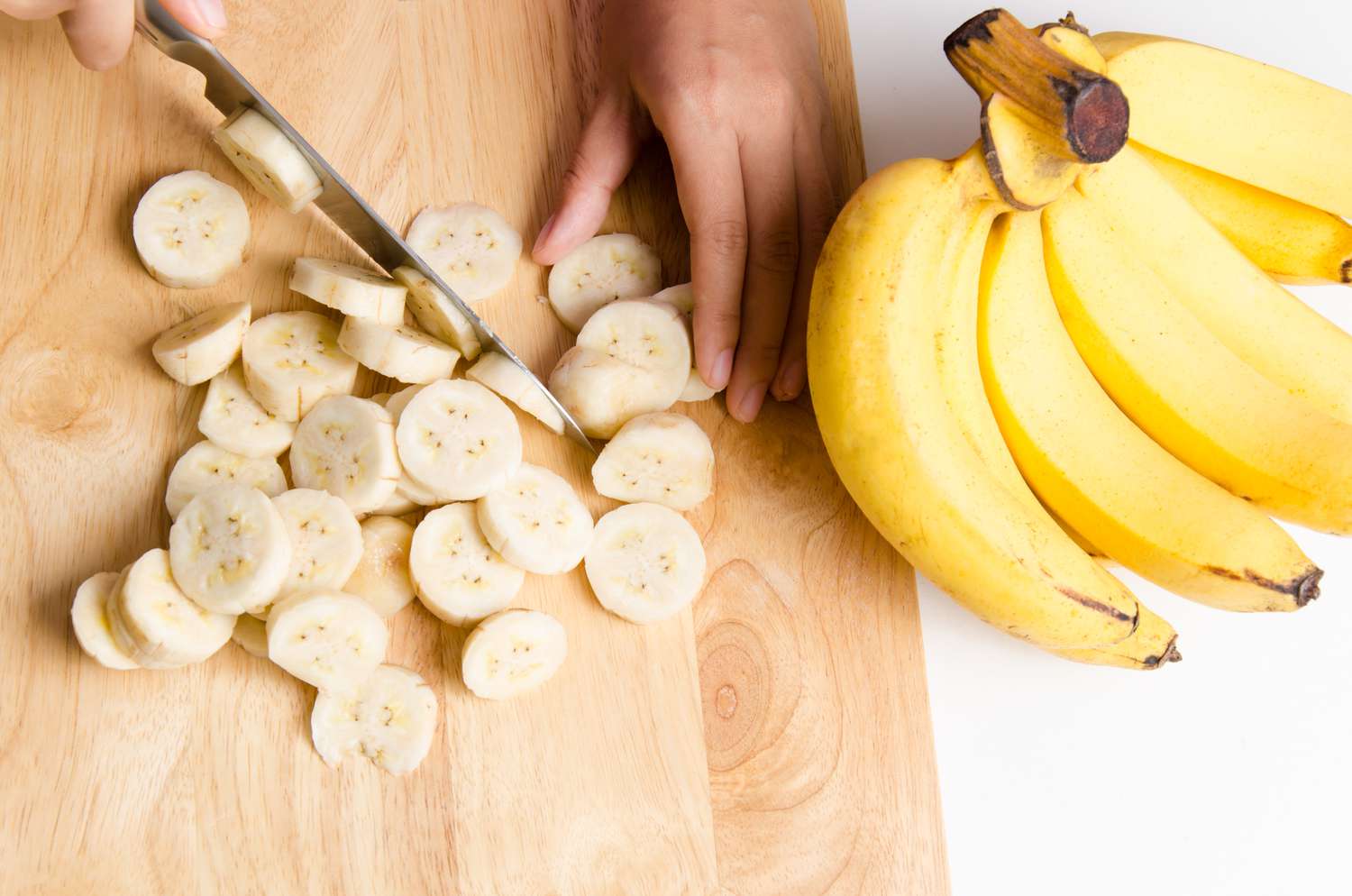 Bijgesneden handen die banaan snijden op snijplank
