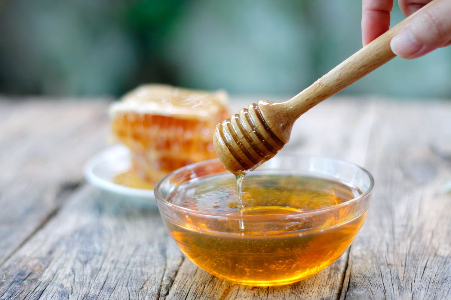 een honingdip onderdompelen in een kom honing met honingraten op de achtergrond