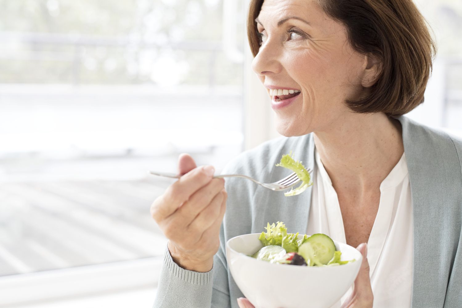 Vrouw die een salade eet, uit het raam kijkt