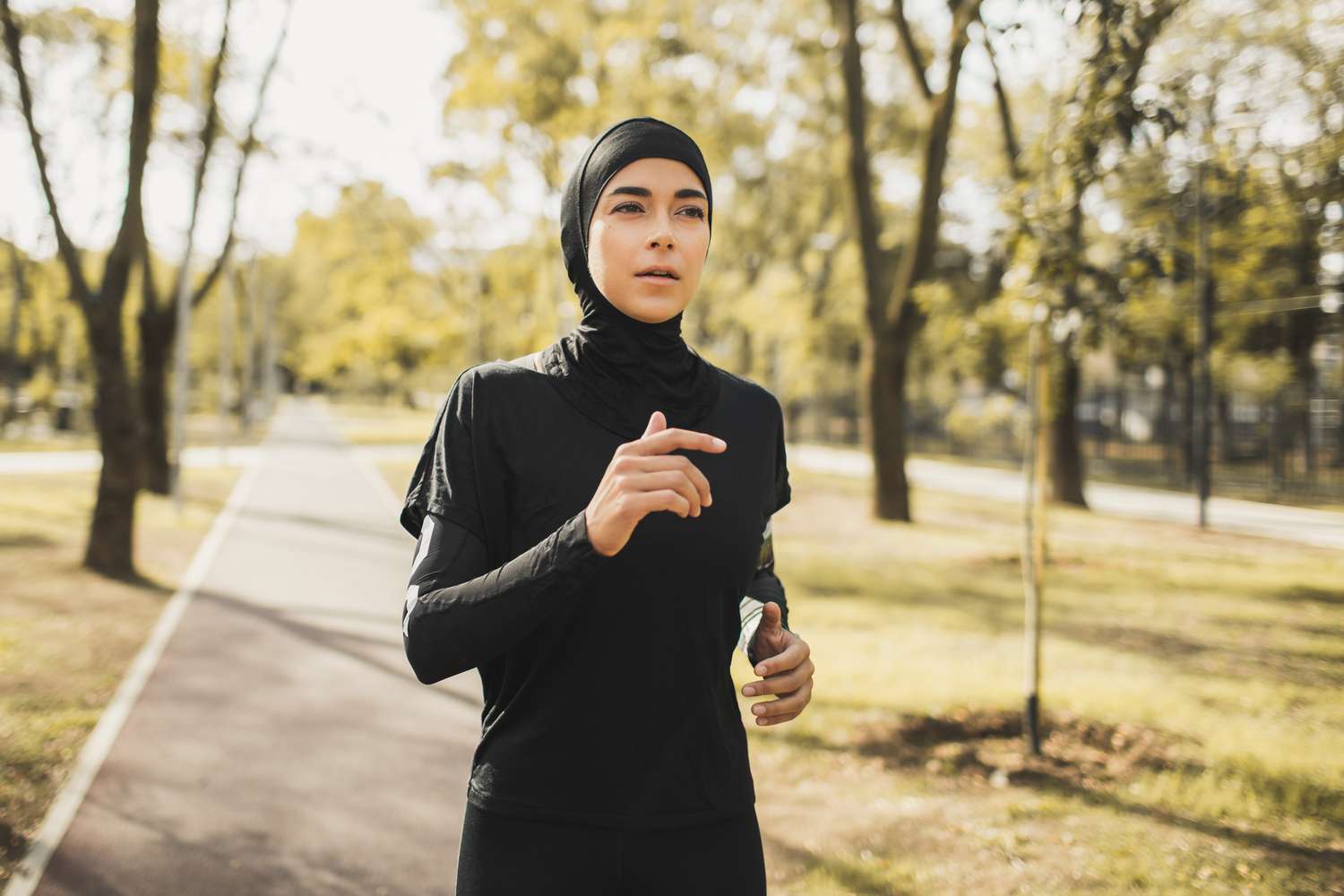 Jonge atletische moslima in zwarte hijab die buiten loopt in herfstpark. Islamitische bescheiden kleding. Arabische vrouw gezonde levensstijl. Buiten joggen. Trainen in het bos. Oosters uiterlijk en kledingstijl.