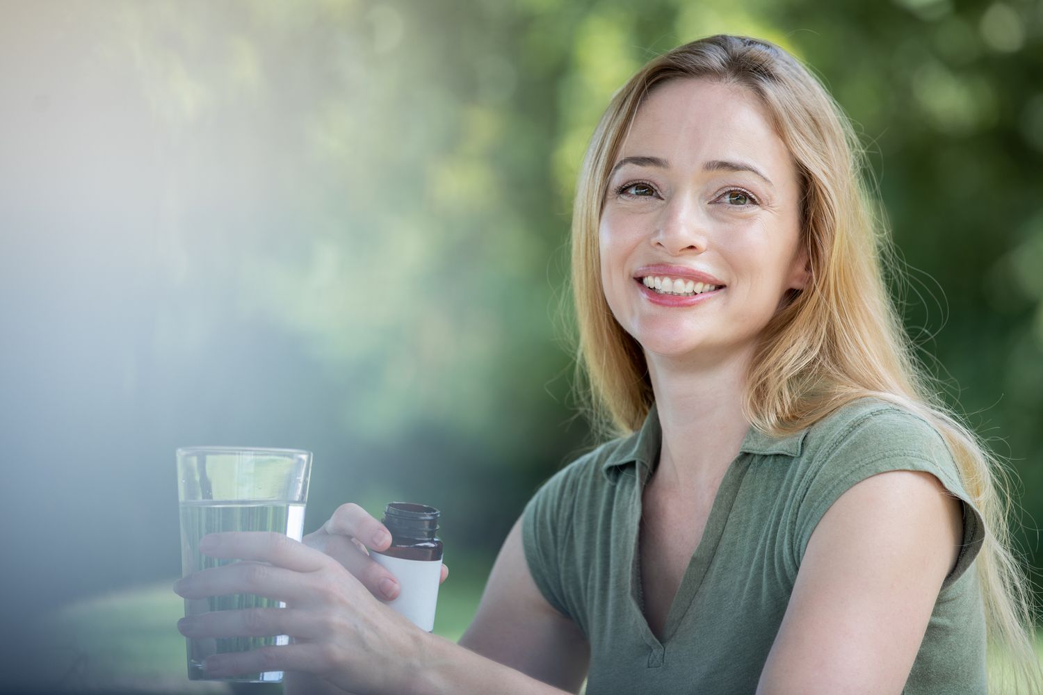 Glimlachende vrouw die collageensupplement en glas water vasthoudt