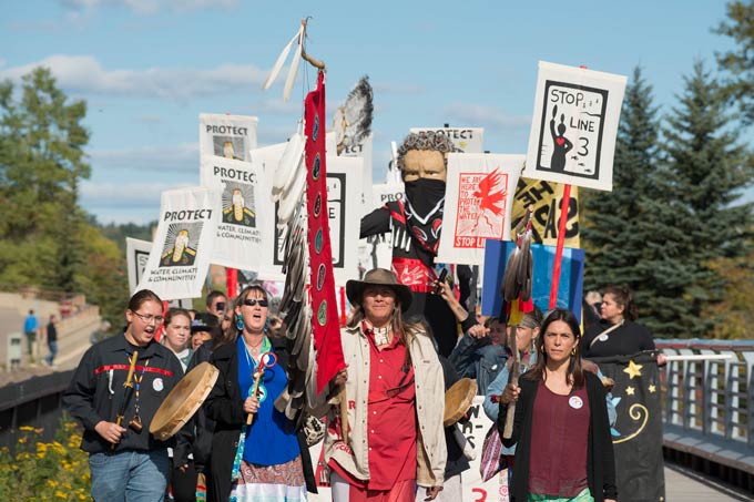 Een groep inheemse leiders marcheert met spandoeken die dingen zeggen als "Halte lijn 3"