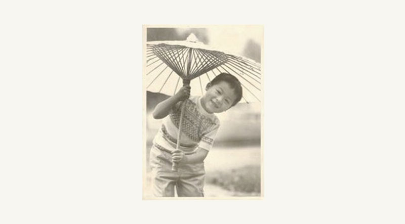 Jason Wang als een jong kind poserend onder een decoratieve paraplu in een vintage foto