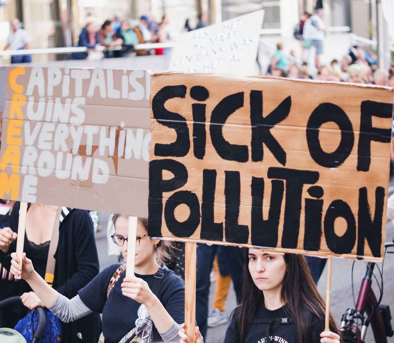 Protestborden met de tekst "Kapitalisme ruïneert alles om me heen" en "Ziek van vervuiling"