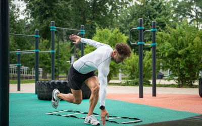 Mannelijke atleet die op één been staat te trainen met snelheidsladder op het sportveld