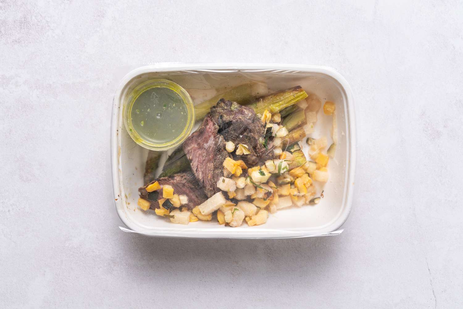 biefstuk, asperges en maïs in een container na het koken