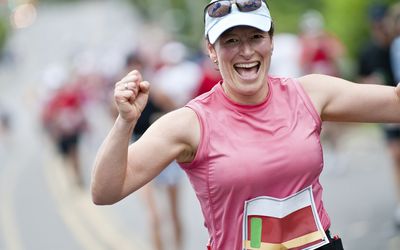 Vrouw glimlacht breed en balt haar vuisten om te vieren dat ze de eerste 30 van de 42 kilometer heeft afgelegd in haar eerste marathonrace.