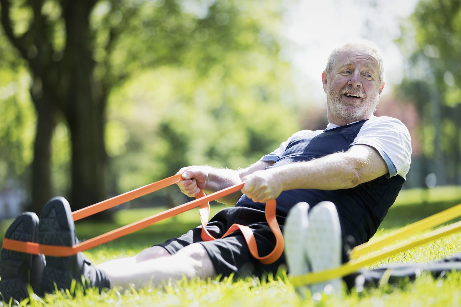 Actieve oudere man die traint in het park, stretcht met weerstandsband