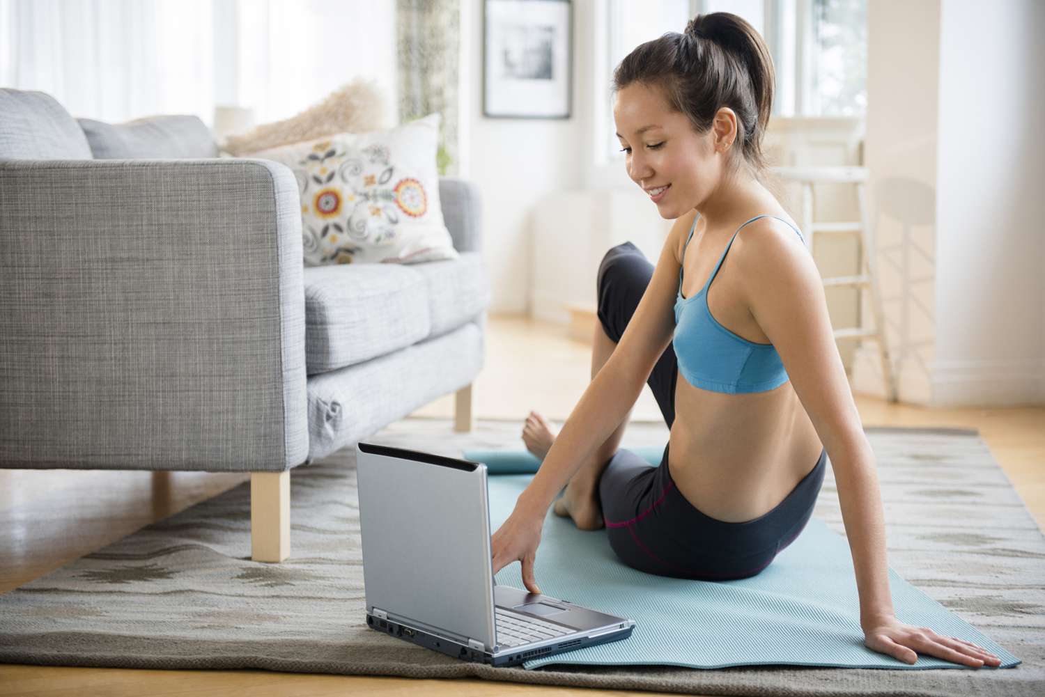 Vrouw in sportbeha en legging op yogamat voor laptop