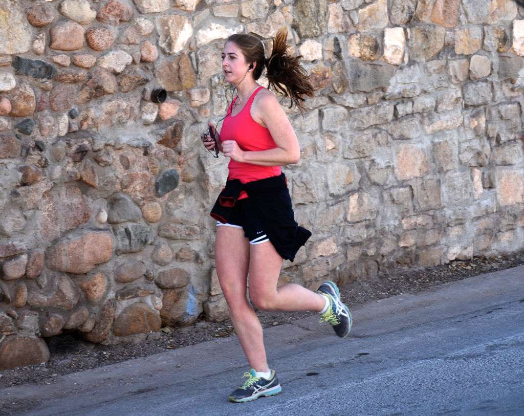Een jonge vrouw gebruikt haar smartphone terwijl ze jogt langs een weg in Santa Fe, New Mexico.